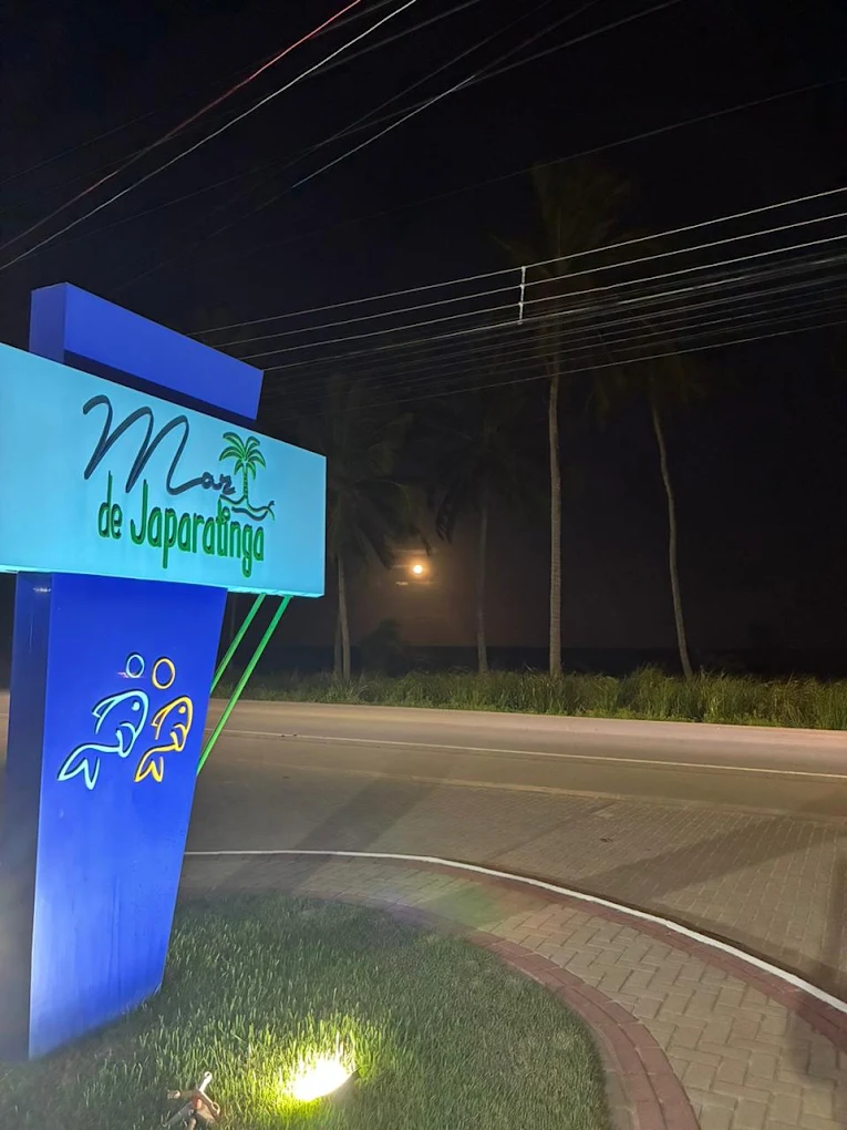 Letreiro iluminado do Mar de Japaratinga à noite com palmeiras